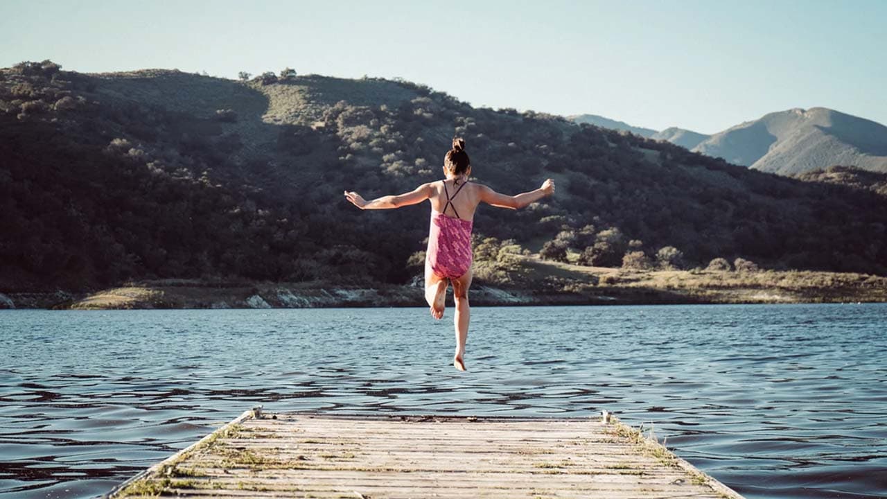 Young girl running and jumping into lake without fear of the unknown