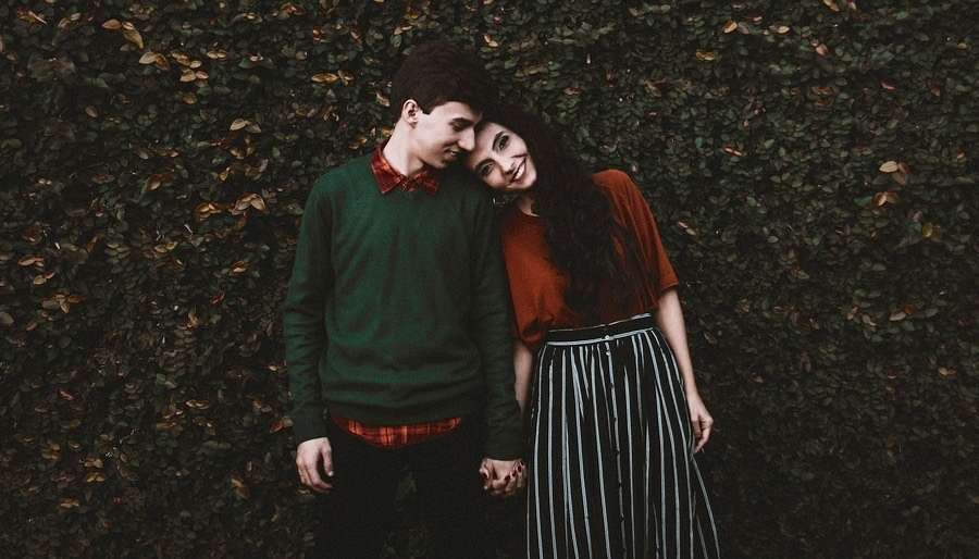 Young cute couple leaning in by hedge