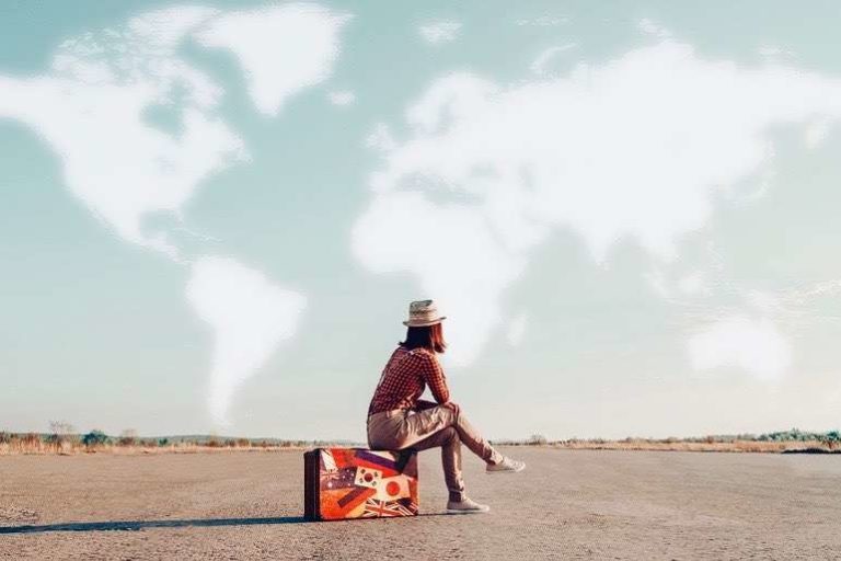 Women Traveler Sitting on case on Airfield, clouds forming map of the world
