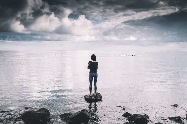 Woman Standing on Empty Beach looking at Horizon