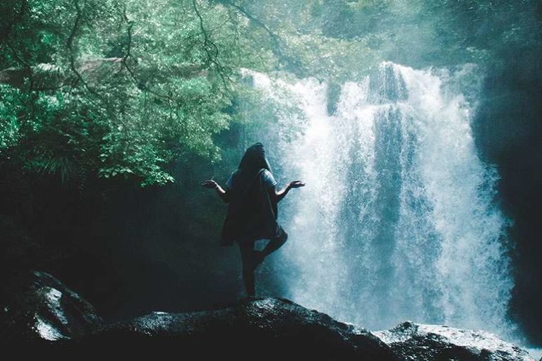Lady standing peacefully in a zen yoga position with a waterfall cascading in front of her